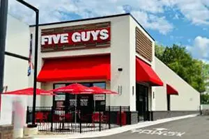 A five guys restaurant with red umbrellas and white walls.