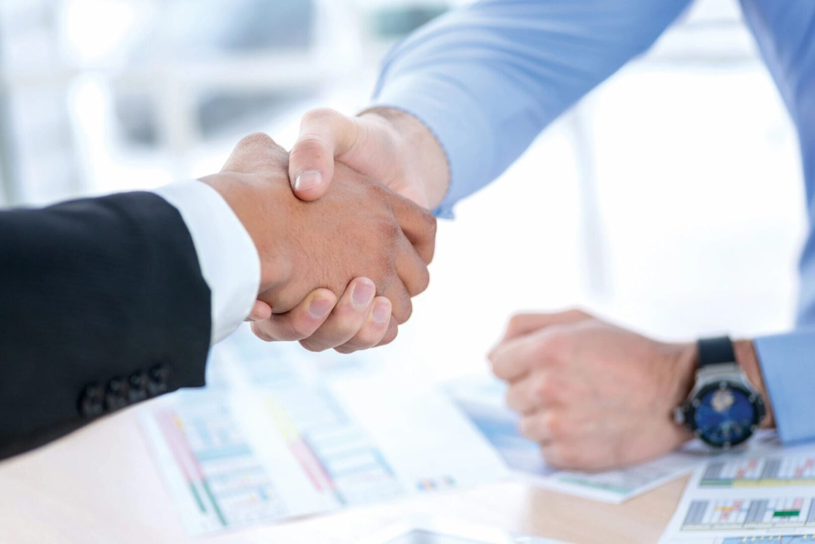 Two people shaking hands over a table.